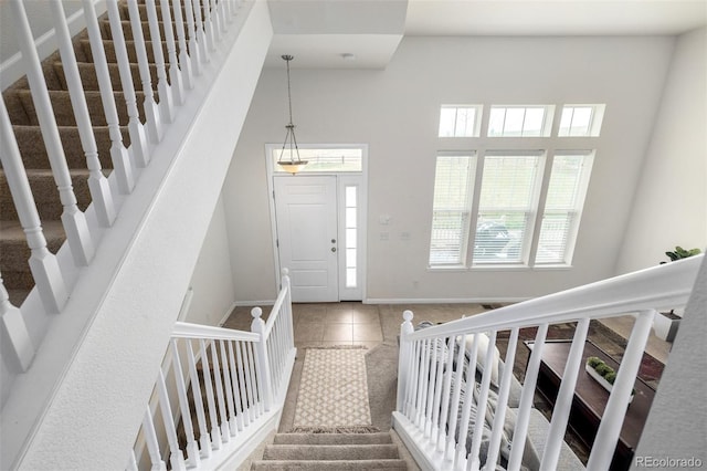 tiled entrance foyer featuring baseboards, stairs, and a high ceiling