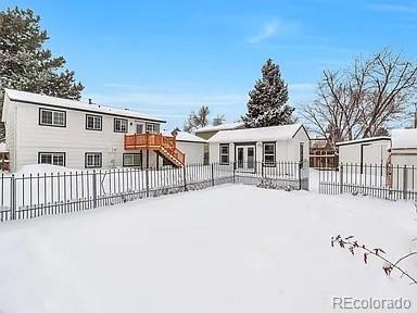 snow covered property featuring an outbuilding, a wooden deck, stairs, and a fenced backyard