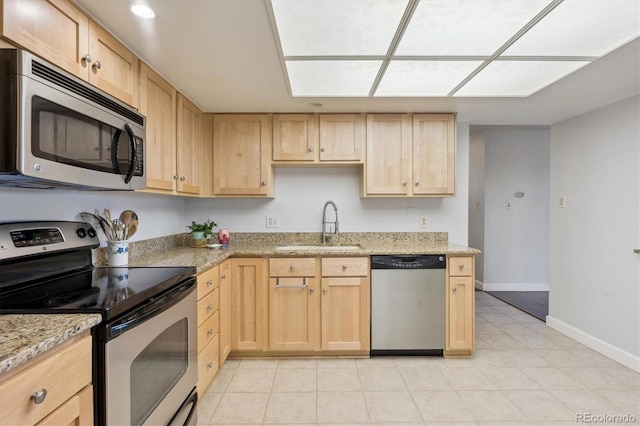 kitchen featuring appliances with stainless steel finishes, light brown cabinetry, a sink, baseboards, and light stone counters