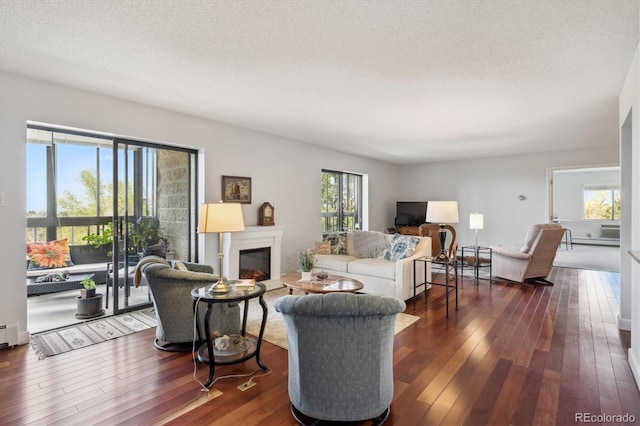 living room featuring dark wood-style floors, a glass covered fireplace, a textured ceiling, and a baseboard heating unit