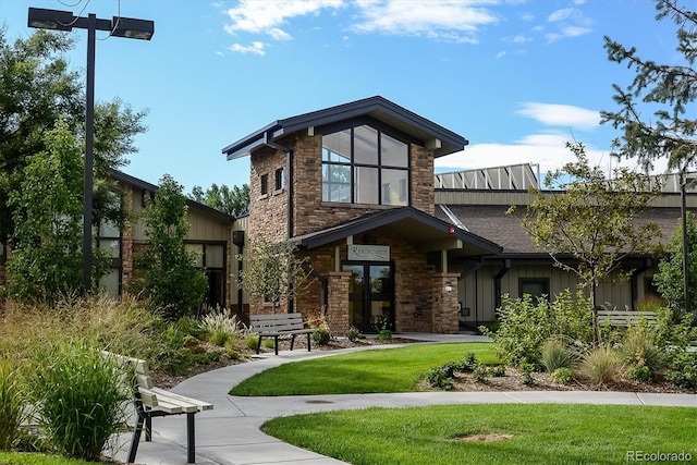 back of property featuring stone siding, a lawn, and board and batten siding