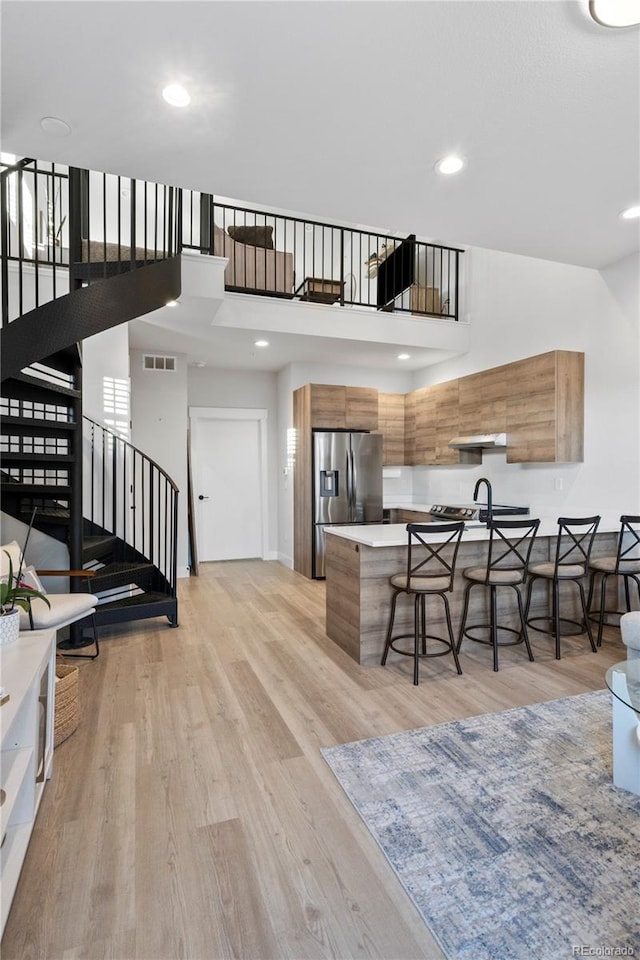 kitchen featuring stainless steel fridge, a breakfast bar, light hardwood / wood-style floors, and a high ceiling