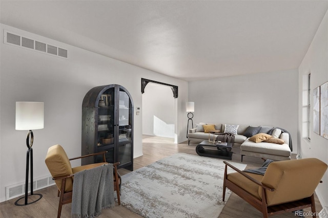 living room with arched walkways, wood finished floors, and visible vents