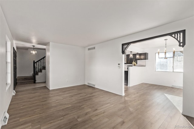 unfurnished living room with a chandelier, stairway, wood finished floors, and visible vents