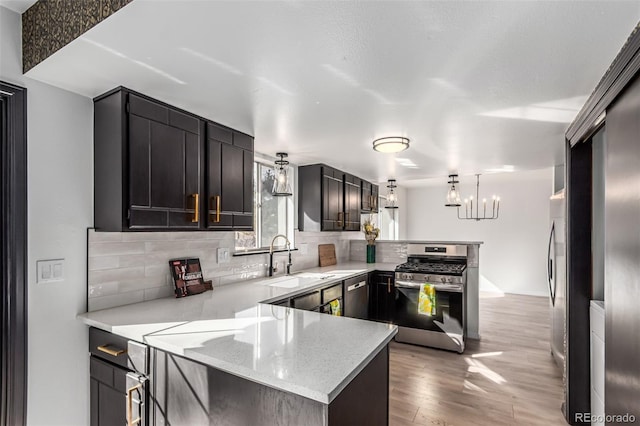 kitchen with appliances with stainless steel finishes, decorative light fixtures, a peninsula, a sink, and backsplash