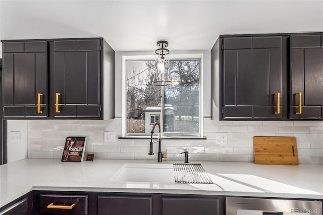 kitchen with light stone counters, a sink, hanging light fixtures, and decorative backsplash