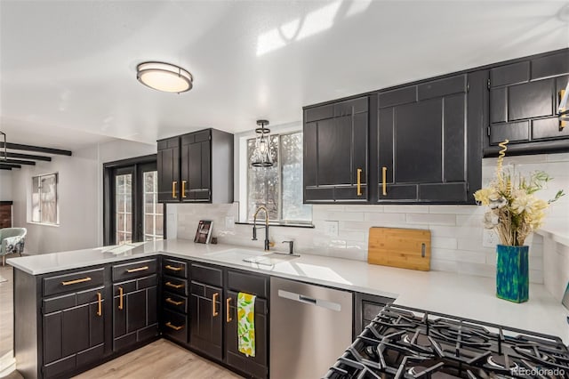 kitchen featuring a sink, light countertops, stainless steel dishwasher, backsplash, and pendant lighting