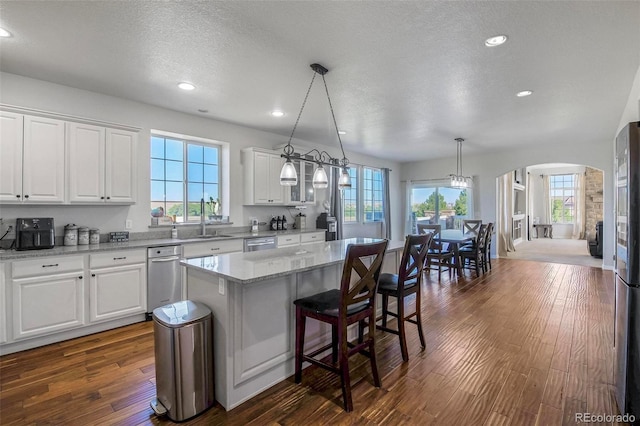 kitchen featuring a healthy amount of sunlight, a kitchen island, hanging light fixtures, dark wood-type flooring, and white cabinets