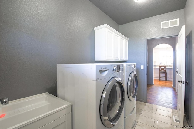 laundry room featuring a textured ceiling, light hardwood / wood-style flooring, washer and dryer, and sink