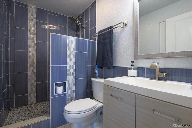 bathroom featuring a textured ceiling, vanity, toilet, and a tile shower