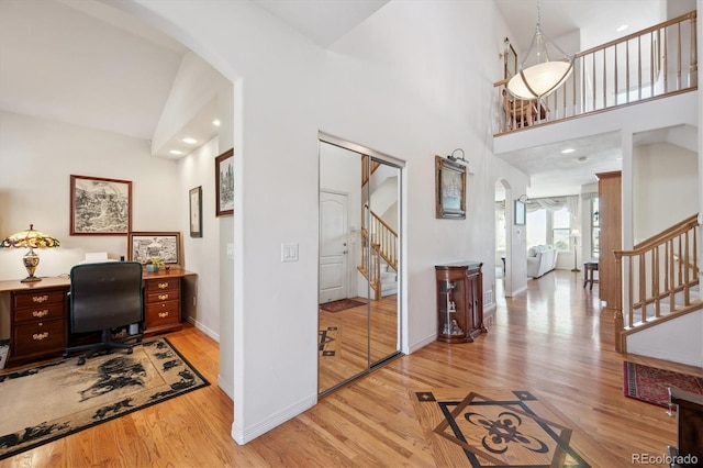 interior space with baseboards, arched walkways, a towering ceiling, and light wood-type flooring