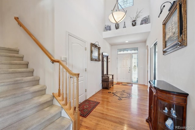 entrance foyer with light wood finished floors, stairway, baseboards, and a towering ceiling