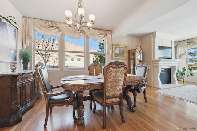 dining room featuring a glass covered fireplace, an inviting chandelier, and light wood-style flooring