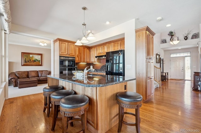 kitchen featuring a sink, a breakfast bar area, black appliances, and light wood-style flooring