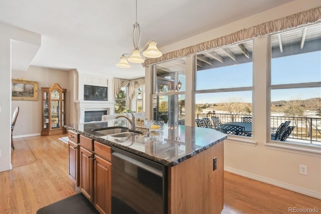 kitchen with light wood-type flooring, dark stone counters, a glass covered fireplace, and a sink