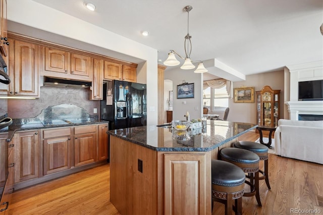 kitchen with black appliances, under cabinet range hood, dark stone countertops, a center island, and a breakfast bar area