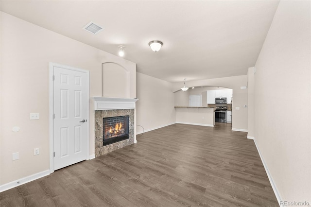 unfurnished living room featuring dark wood-style flooring, a tiled fireplace, baseboards, and arched walkways