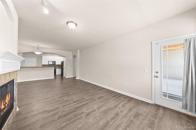 unfurnished living room with dark wood-style flooring, arched walkways, a glass covered fireplace, and baseboards