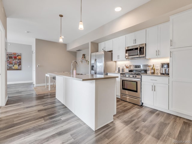 kitchen featuring white cabinetry, an island with sink, sink, hanging light fixtures, and stainless steel appliances