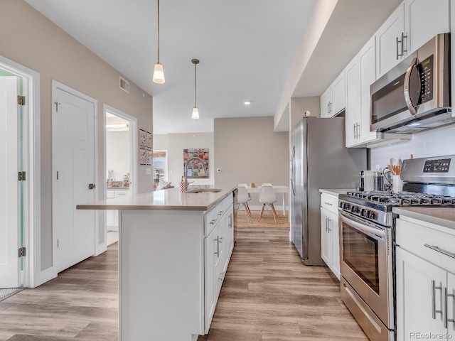 kitchen featuring appliances with stainless steel finishes, pendant lighting, sink, white cabinets, and a kitchen island with sink