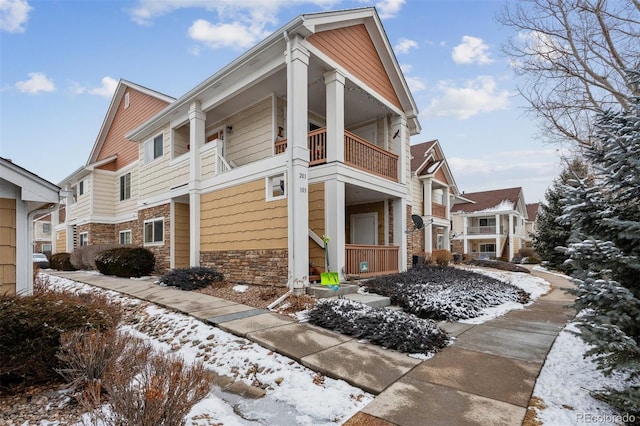 snow covered property with a balcony and stone siding