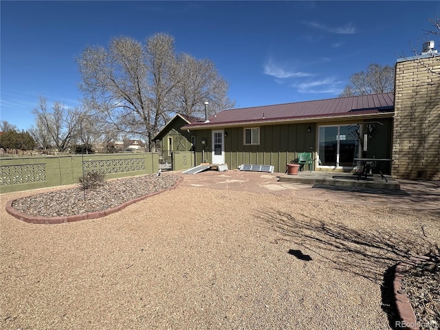 back of property featuring a patio, fence, board and batten siding, metal roof, and a chimney