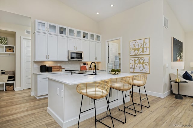 kitchen with stainless steel appliances, a kitchen island with sink, light stone countertops, white cabinetry, and light wood-type flooring