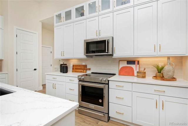 kitchen featuring light stone counters, white cabinetry, light wood-type flooring, and appliances with stainless steel finishes