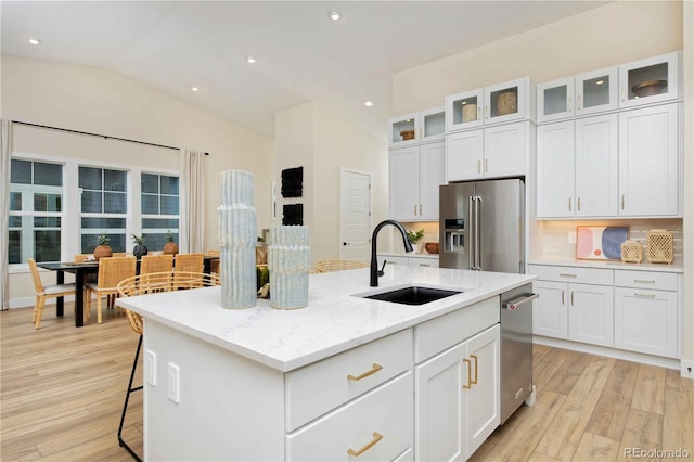 kitchen featuring stainless steel appliances, light stone countertops, sink, an island with sink, and light hardwood / wood-style floors