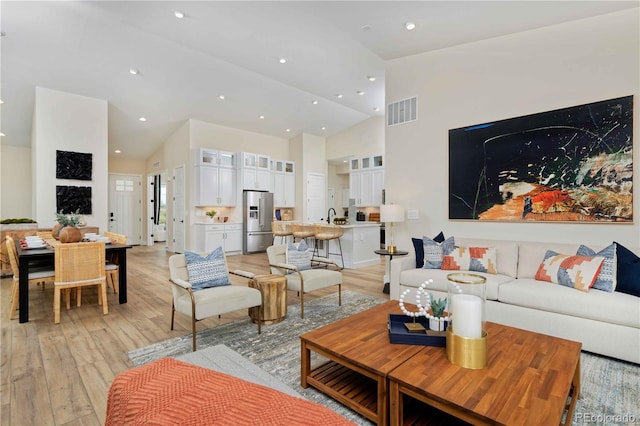 living room with sink, light hardwood / wood-style flooring, and high vaulted ceiling