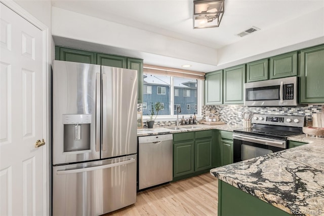 kitchen featuring stainless steel appliances, green cabinets, light hardwood / wood-style floors, and sink