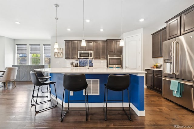 kitchen featuring stainless steel appliances, a center island with sink, dark brown cabinetry, and decorative light fixtures