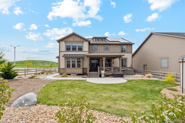 back of property featuring a hot tub, a lawn, solar panels, and a patio