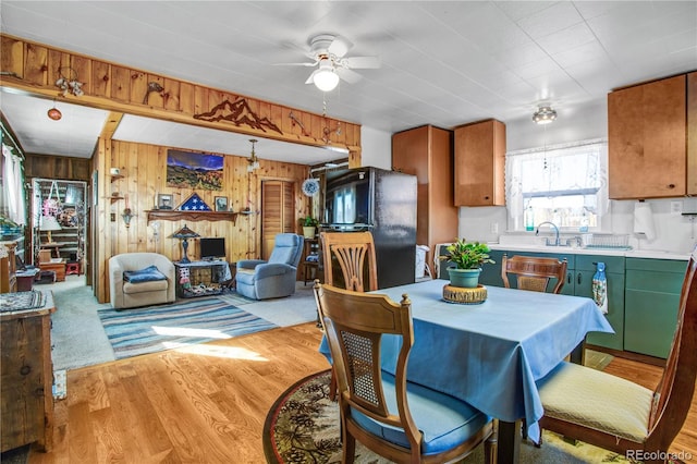 dining area with ceiling fan, wooden walls, sink, and light hardwood / wood-style flooring