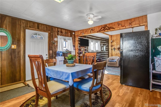 dining space featuring light hardwood / wood-style flooring, wooden walls, and ceiling fan