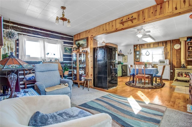 living room featuring ceiling fan, light wood-type flooring, a wood stove, and wood walls