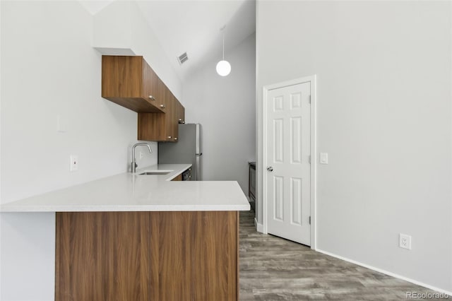 kitchen with a sink, light countertops, a peninsula, wood finished floors, and brown cabinets