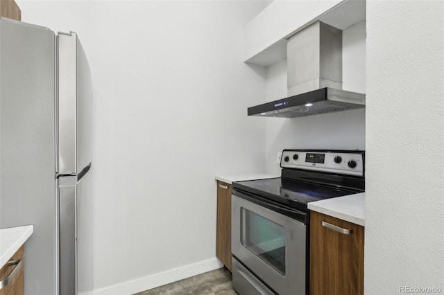 kitchen with appliances with stainless steel finishes, wall chimney range hood, light countertops, baseboards, and light wood-style flooring