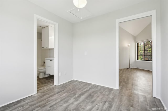 empty room with wood finished floors, vaulted ceiling, baseboards, and attic access