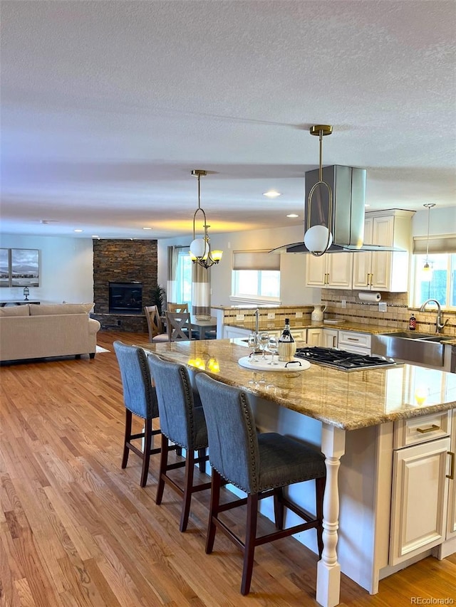 kitchen featuring sink, backsplash, hanging light fixtures, and a stone fireplace