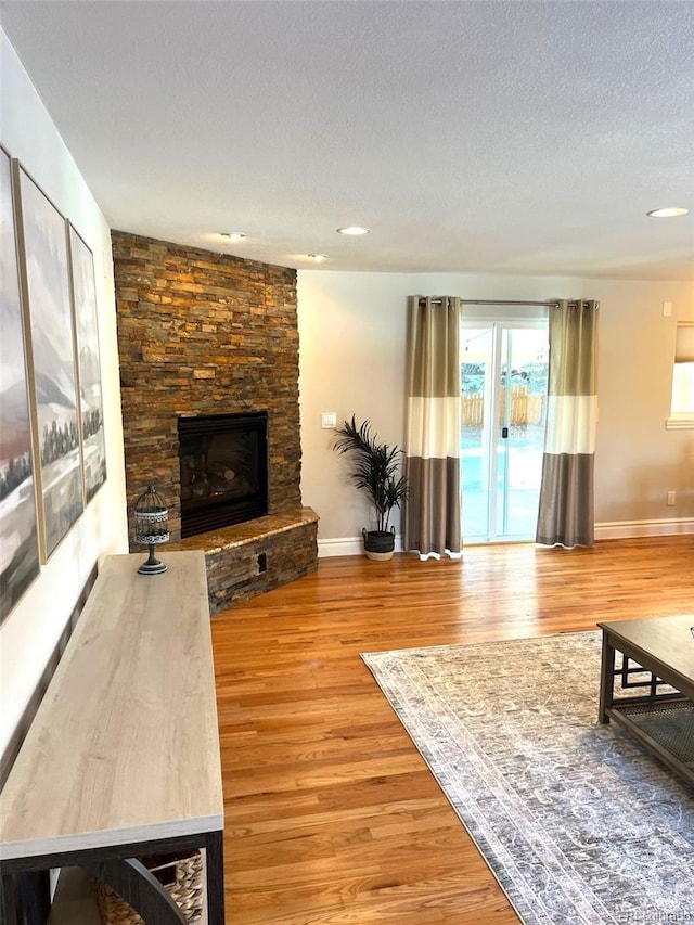 living room with wood-type flooring, a textured ceiling, and a stone fireplace