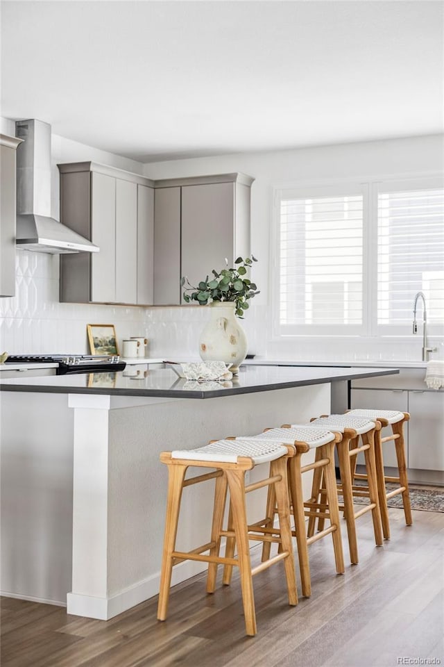 15006 Cast Pebble Cir, Parker, CO 80134 - kitchen with wall chimney exhaust hood, gray cabinets, wood finished floors, a kitchen breakfast bar, and tasteful backsplash