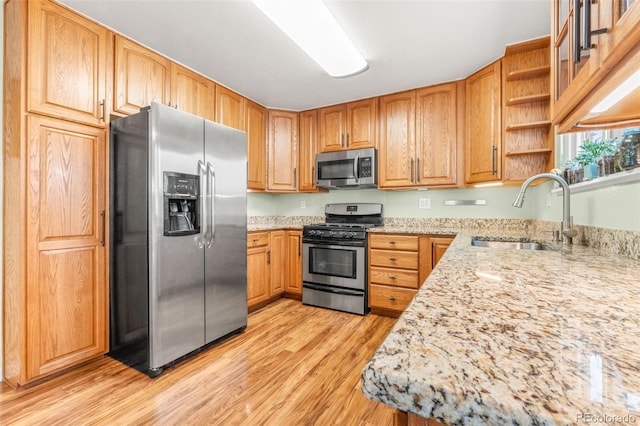 kitchen with light wood finished floors, light stone counters, stainless steel appliances, open shelves, and a sink