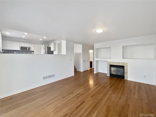 unfurnished living room with a tiled fireplace and hardwood / wood-style floors