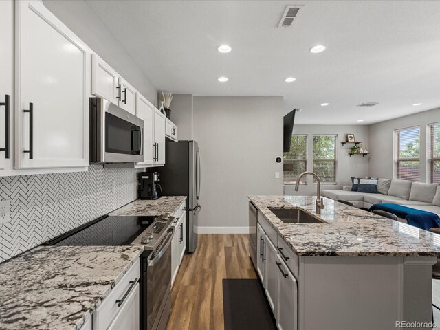 14823 W 70th Dr Unit A, Arvada, CO 80007 - kitchen featuring stainless steel appliances, a sink, open floor plan, a kitchen island with sink, and tasteful backsplash