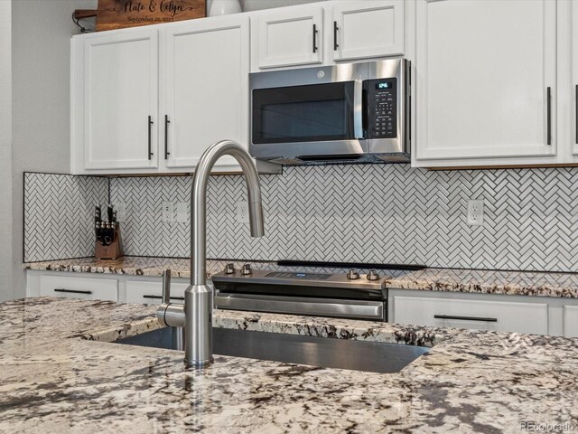 14823 W 70th Dr Unit A, Arvada, CO 80007 - kitchen featuring stainless steel microwave, backsplash, white cabinetry, light stone countertops, and a sink