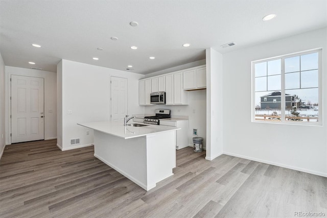 kitchen featuring white cabinetry, sink, stainless steel appliances, light hardwood / wood-style flooring, and an island with sink