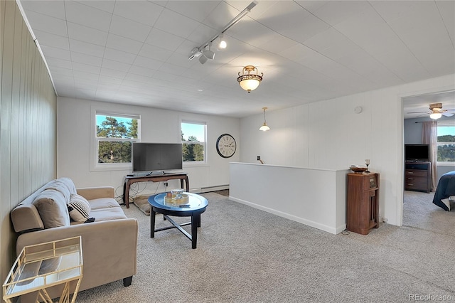 carpeted living room with ceiling fan, rail lighting, a baseboard heating unit, and a healthy amount of sunlight