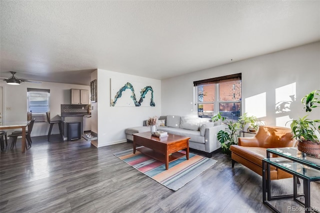 living room featuring ceiling fan, dark wood-type flooring, and a textured ceiling