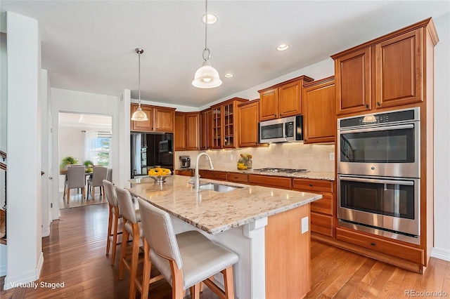 26004 E Elmhurst Pl, Aurora, CO 80016 - kitchen featuring appliances with stainless steel finishes, a sink, brown cabinetry, light wood-style flooring, and light stone countertops